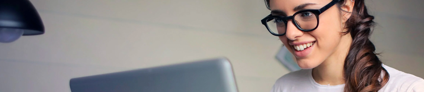 women with glasses smiling and looking at her laptop